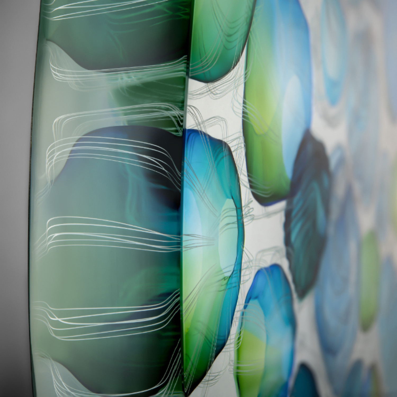 A close up of a hand crafted piece of art made of glass. Green and blue, jellyfish like abstract shapes appear in the clear glass.